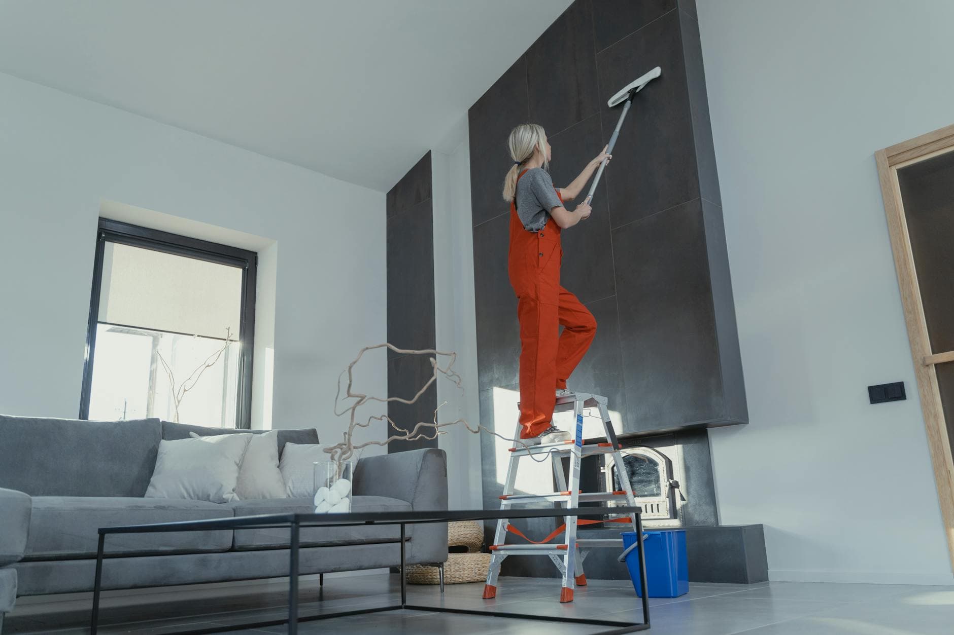 New York Maid cleaner in red overalls on a ladder cleaning a high wall in a Westchester apartment — Office Cleaning in Bronxville, Westchester County