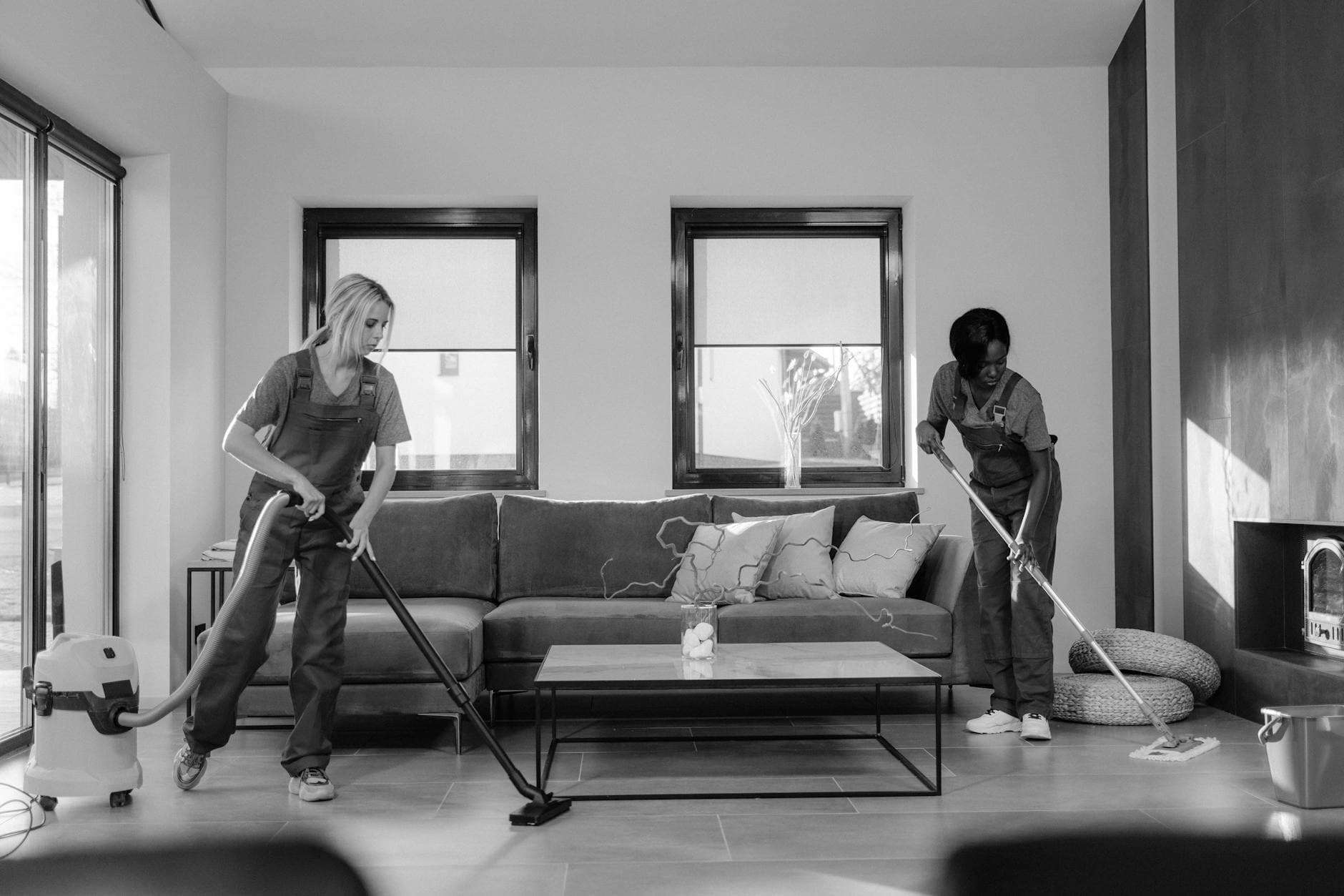 Two New York Maid cleaners in work uniforms using a vacuum and mop in a modern Westchester living room — Move-In/Move-Out Cleaning in Mount Vernon, Westchester County